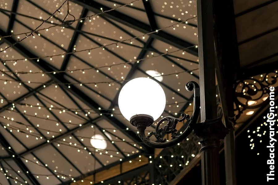 White round lantern on a wrought iron pillar of the restaurant terrace gazebo with garlands on the ceiling, architectural lighting of the room in a retro style